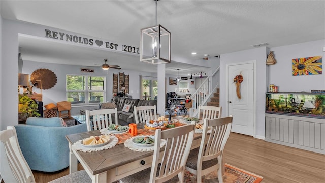 dining area with light wood-type flooring, ceiling fan with notable chandelier, and a textured ceiling