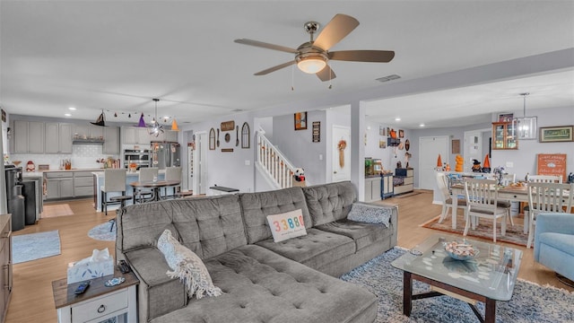 living room with ceiling fan with notable chandelier and light hardwood / wood-style floors