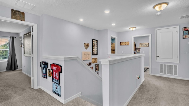 hall with a textured ceiling and light colored carpet