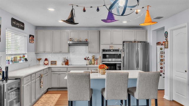 kitchen with light wood-type flooring, beverage cooler, gray cabinetry, stainless steel appliances, and exhaust hood