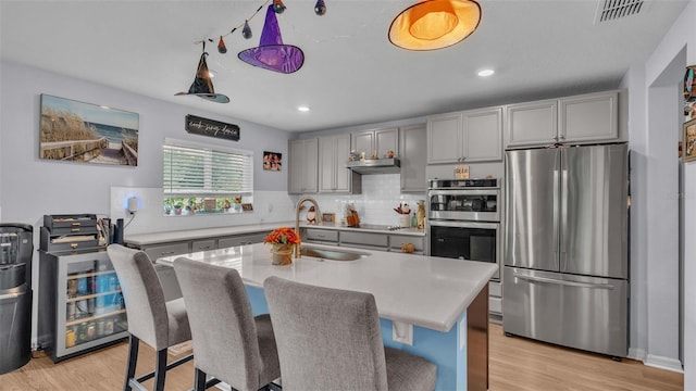 kitchen with appliances with stainless steel finishes, decorative backsplash, light hardwood / wood-style floors, and sink