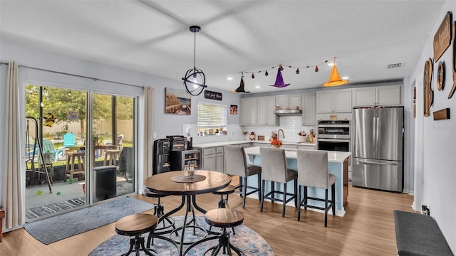 kitchen featuring hanging light fixtures, decorative backsplash, gray cabinets, stainless steel appliances, and light hardwood / wood-style flooring