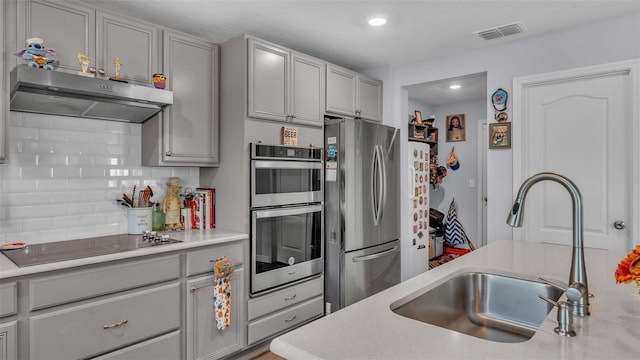 kitchen with appliances with stainless steel finishes, gray cabinetry, decorative backsplash, and sink