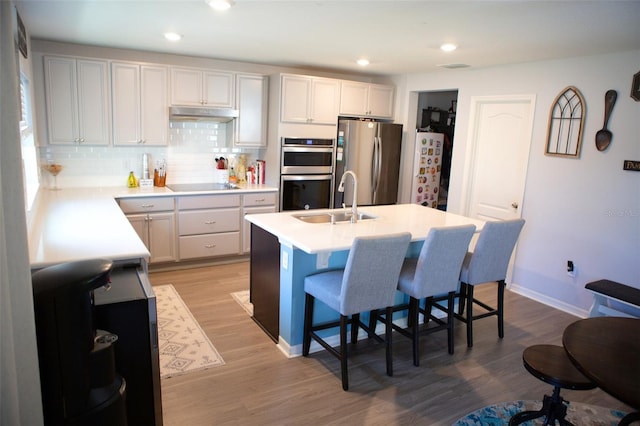 kitchen featuring under cabinet range hood, a sink, a kitchen breakfast bar, stainless steel appliances, and light wood-style floors