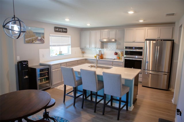 kitchen with visible vents, a sink, stainless steel appliances, under cabinet range hood, and tasteful backsplash