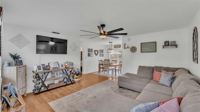 living room with light hardwood / wood-style floors and ceiling fan with notable chandelier