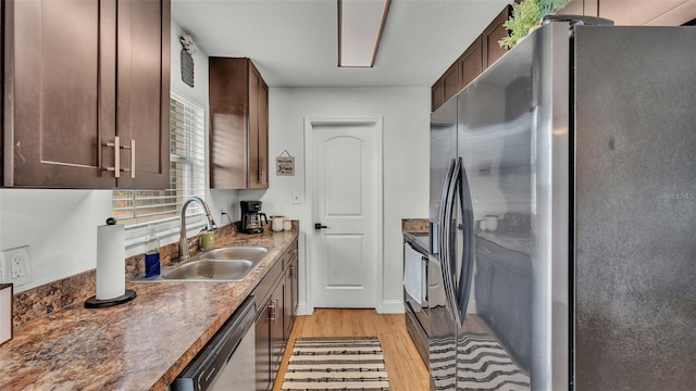 kitchen with stainless steel appliances, dark stone countertops, sink, dark brown cabinetry, and light hardwood / wood-style floors