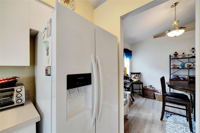 kitchen with hanging light fixtures, light hardwood / wood-style floors, white fridge with ice dispenser, and white cabinets