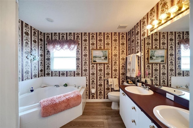 bathroom with hardwood / wood-style floors, vanity, tiled bath, and toilet