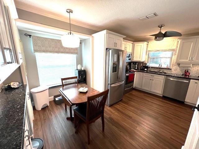 kitchen with dark wood-type flooring, hanging light fixtures, tasteful backsplash, white cabinetry, and stainless steel appliances