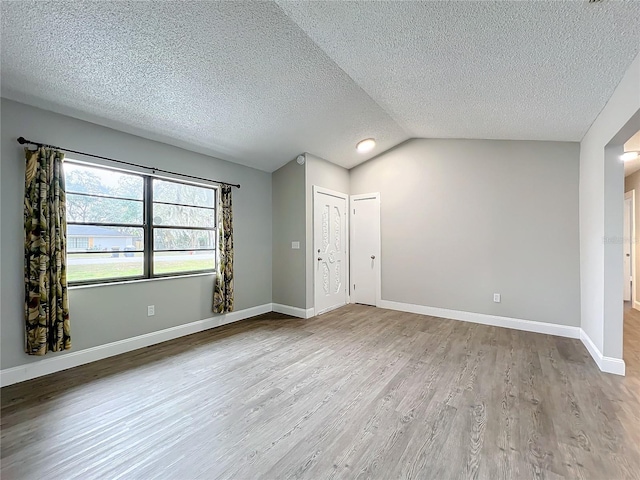 unfurnished room featuring a textured ceiling, light hardwood / wood-style floors, and lofted ceiling