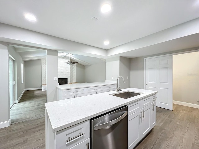 kitchen with a kitchen island with sink, sink, stainless steel dishwasher, a fireplace, and white cabinetry