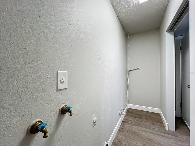 clothes washing area with hookup for an electric dryer, a textured ceiling, and hardwood / wood-style flooring