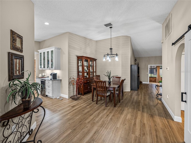 dining area featuring wine cooler, a barn door, an inviting chandelier, light hardwood / wood-style flooring, and a textured ceiling