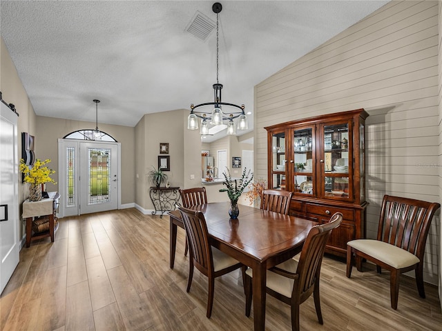 dining space featuring an inviting chandelier, a barn door, wood walls, hardwood / wood-style floors, and lofted ceiling