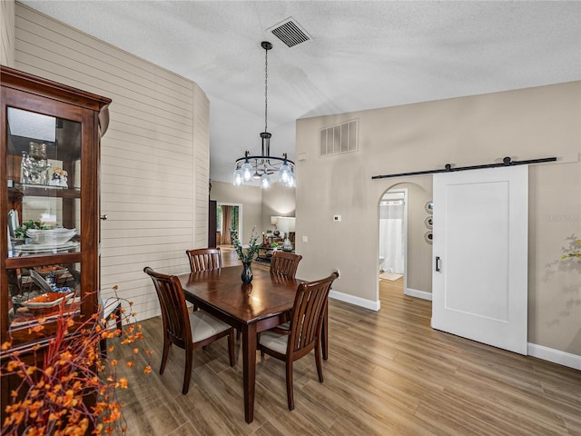 dining space featuring a barn door, hardwood / wood-style flooring, wooden walls, vaulted ceiling, and a textured ceiling