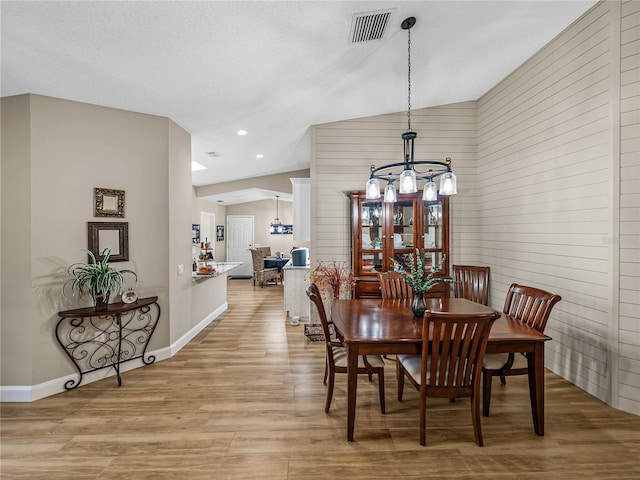 dining area featuring light hardwood / wood-style floors, lofted ceiling, a chandelier, and wooden walls