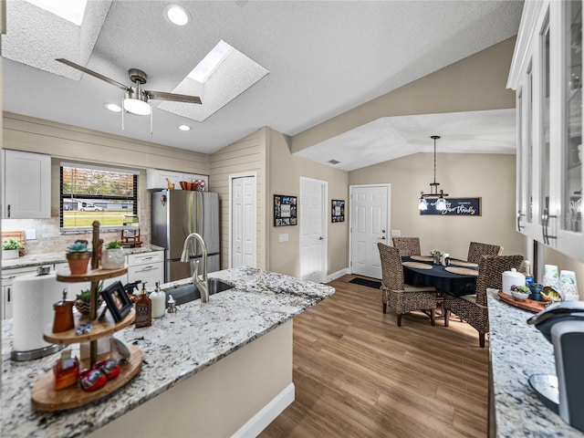 kitchen with white cabinetry, stainless steel fridge, decorative light fixtures, vaulted ceiling with skylight, and a textured ceiling