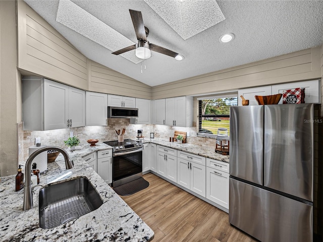 kitchen featuring white cabinetry, stainless steel appliances, lofted ceiling with skylight, light stone countertops, and sink