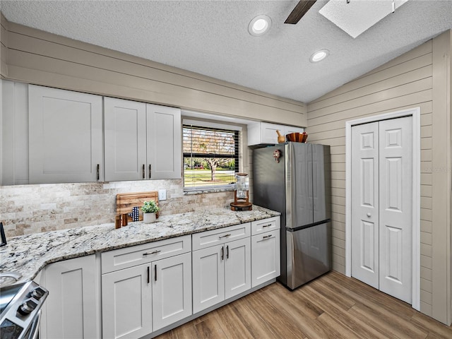 kitchen featuring white cabinetry, appliances with stainless steel finishes, light wood-type flooring, a textured ceiling, and light stone counters