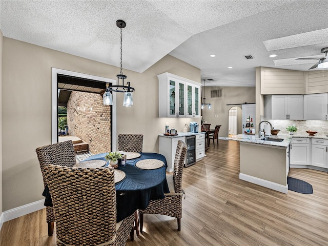 dining room featuring ceiling fan, beverage cooler, a textured ceiling, light hardwood / wood-style flooring, and sink