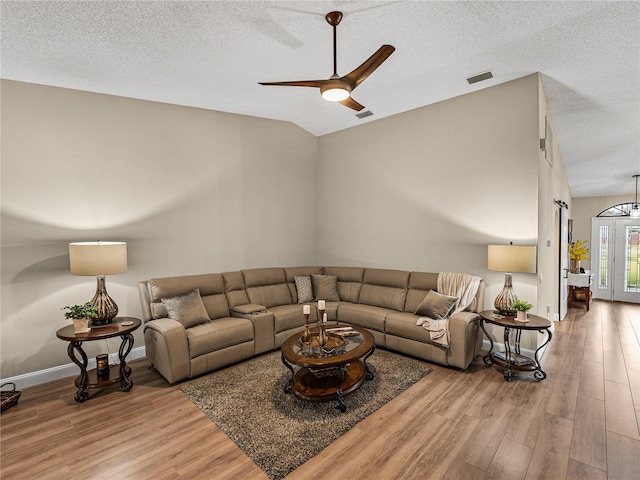 living room featuring ceiling fan, light wood-type flooring, vaulted ceiling, and a textured ceiling