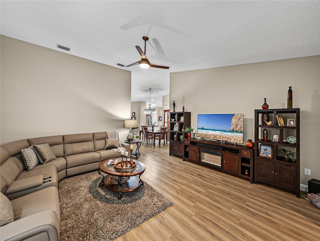 living room with hardwood / wood-style flooring, a textured ceiling, vaulted ceiling, and ceiling fan with notable chandelier