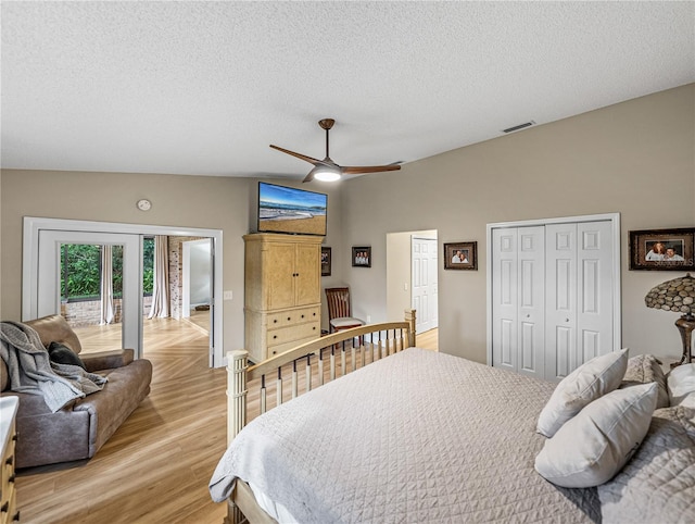 bedroom with ceiling fan, multiple closets, vaulted ceiling, light wood-type flooring, and a textured ceiling