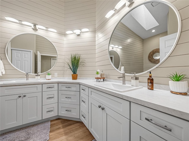 bathroom with lofted ceiling with skylight, hardwood / wood-style floors, vanity, and wood walls