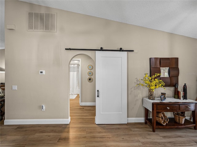 interior space with vaulted ceiling, a barn door, and wood-type flooring