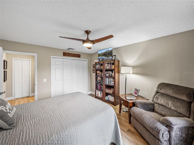 bedroom with ceiling fan, light hardwood / wood-style floors, a textured ceiling, and a closet