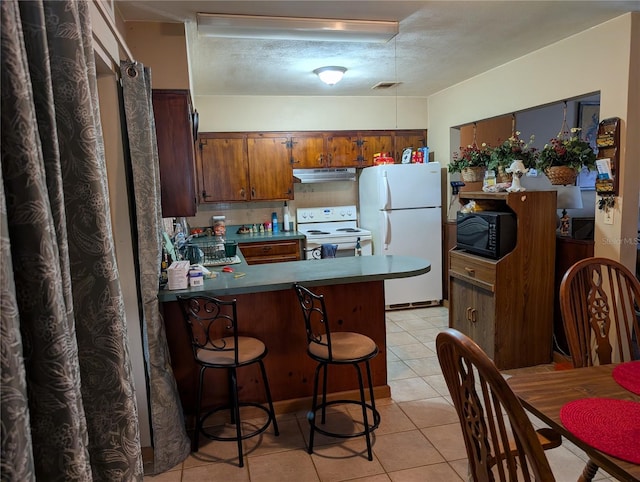 kitchen with light tile patterned flooring, white appliances, and kitchen peninsula