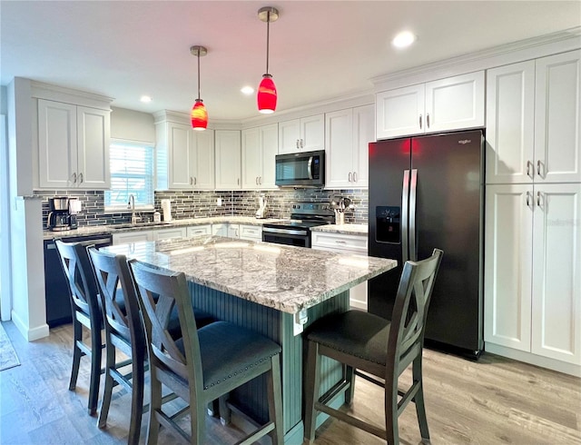 kitchen with hanging light fixtures, appliances with stainless steel finishes, a kitchen breakfast bar, a kitchen island, and white cabinets