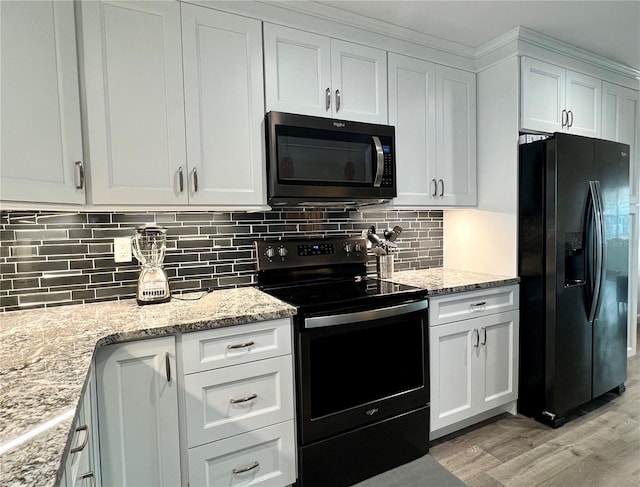 kitchen featuring tasteful backsplash, white cabinets, black appliances, light stone countertops, and light hardwood / wood-style flooring