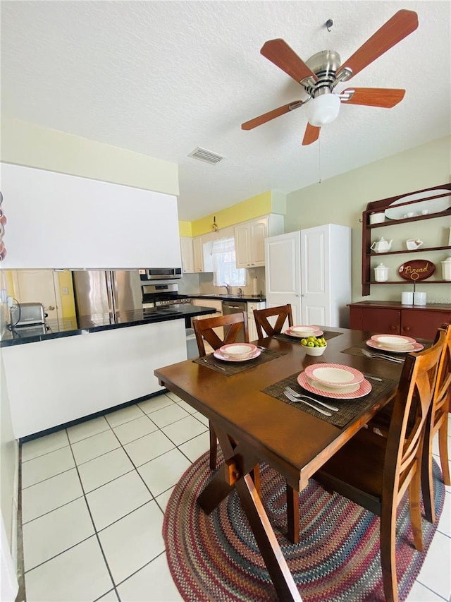 dining space featuring light tile patterned flooring, ceiling fan, and a textured ceiling