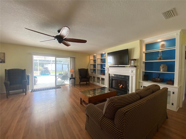 living room with hardwood / wood-style flooring, ceiling fan, a high end fireplace, a textured ceiling, and built in shelves