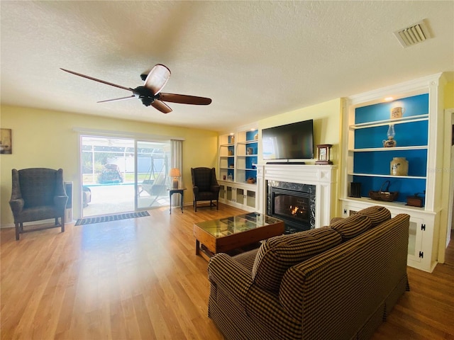 living room featuring hardwood / wood-style flooring, built in features, a premium fireplace, and a textured ceiling