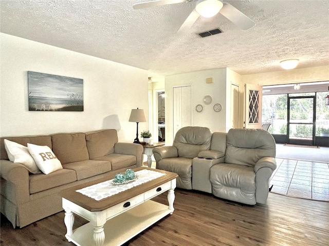 living area with a textured ceiling, dark wood-style flooring, visible vents, and a ceiling fan