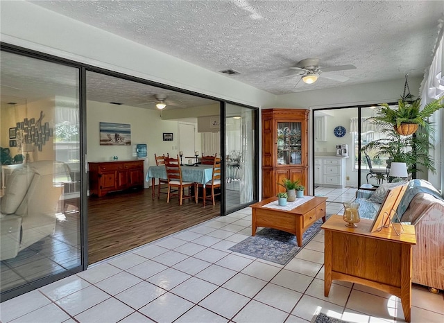 living area with light tile patterned floors, a textured ceiling, visible vents, and a ceiling fan