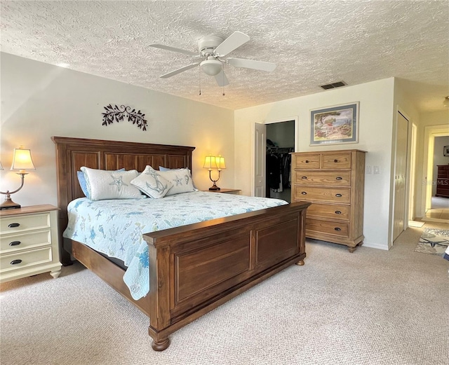 bedroom with a textured ceiling, ceiling fan, light colored carpet, visible vents, and a closet