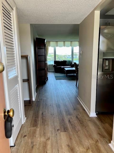 hall with a textured ceiling, wood finished floors, and baseboards