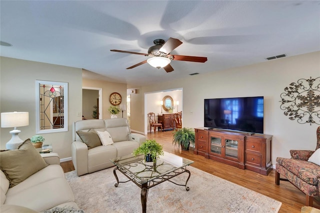 living room featuring light wood-type flooring, ceiling fan, visible vents, and baseboards