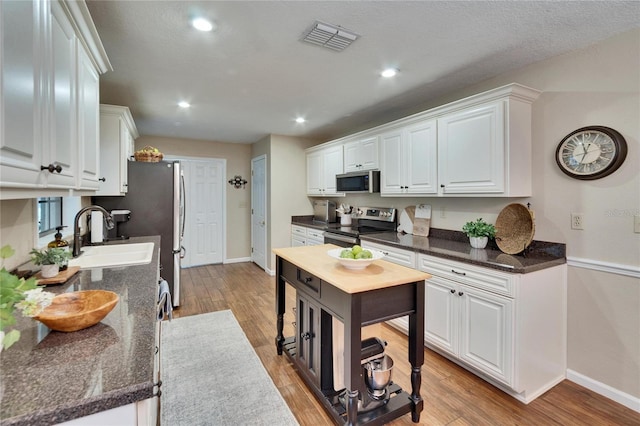 kitchen with appliances with stainless steel finishes, white cabinets, a sink, and visible vents