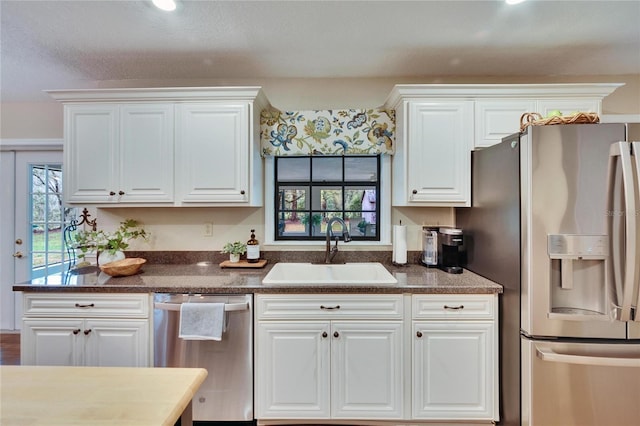 kitchen with appliances with stainless steel finishes, dark countertops, white cabinets, and a sink