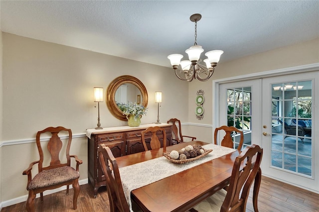 dining room with a textured ceiling, wood finished floors, baseboards, french doors, and an inviting chandelier