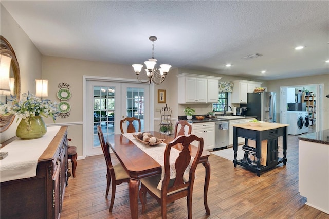 dining area featuring washing machine and clothes dryer, an inviting chandelier, a textured ceiling, french doors, and light wood-type flooring