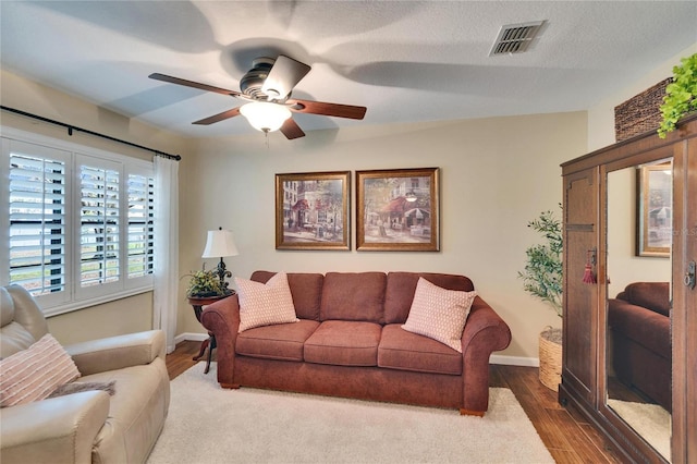 living area featuring a textured ceiling, ceiling fan, wood finished floors, visible vents, and baseboards