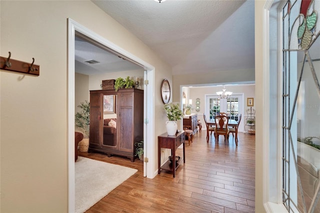 foyer entrance with a notable chandelier, a textured ceiling, visible vents, and wood finished floors