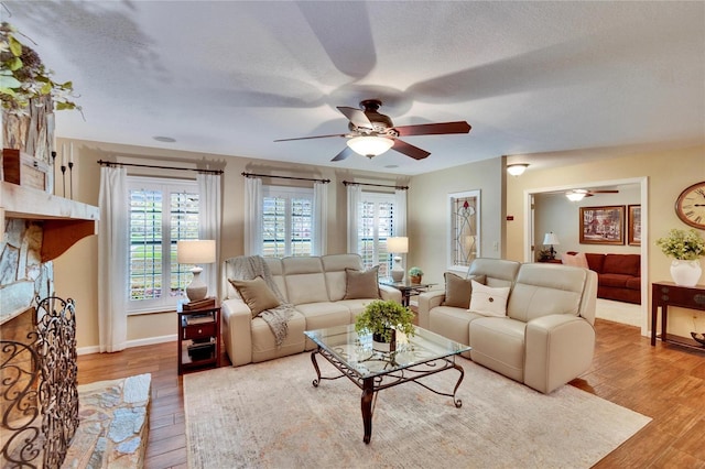 living room featuring a textured ceiling, light wood-type flooring, a ceiling fan, and baseboards