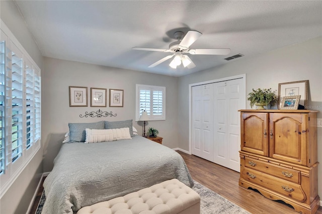 bedroom with a closet, visible vents, a ceiling fan, wood finished floors, and baseboards